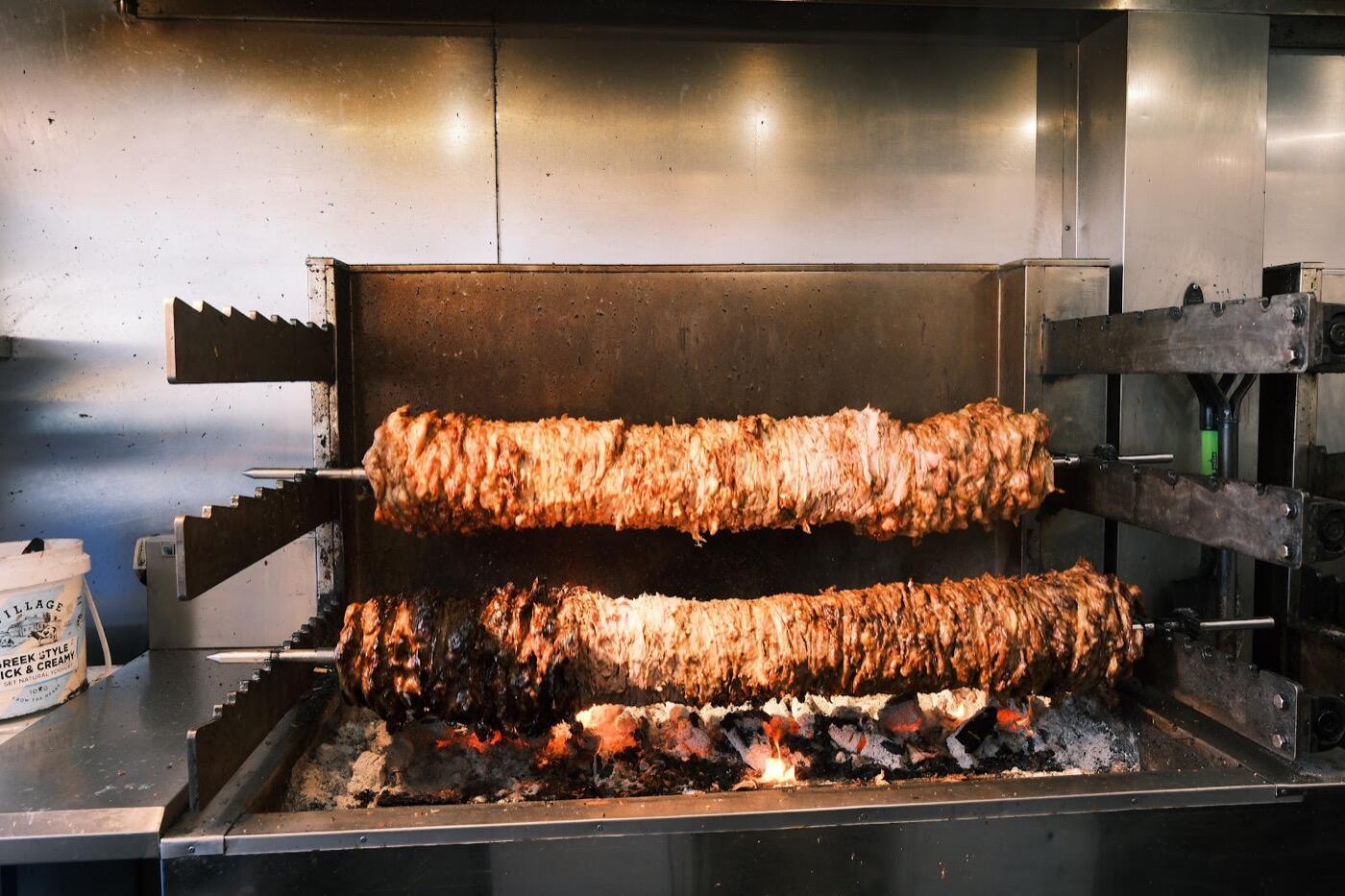 Two large rotating spits of meat above glowing charcoal in the open grill