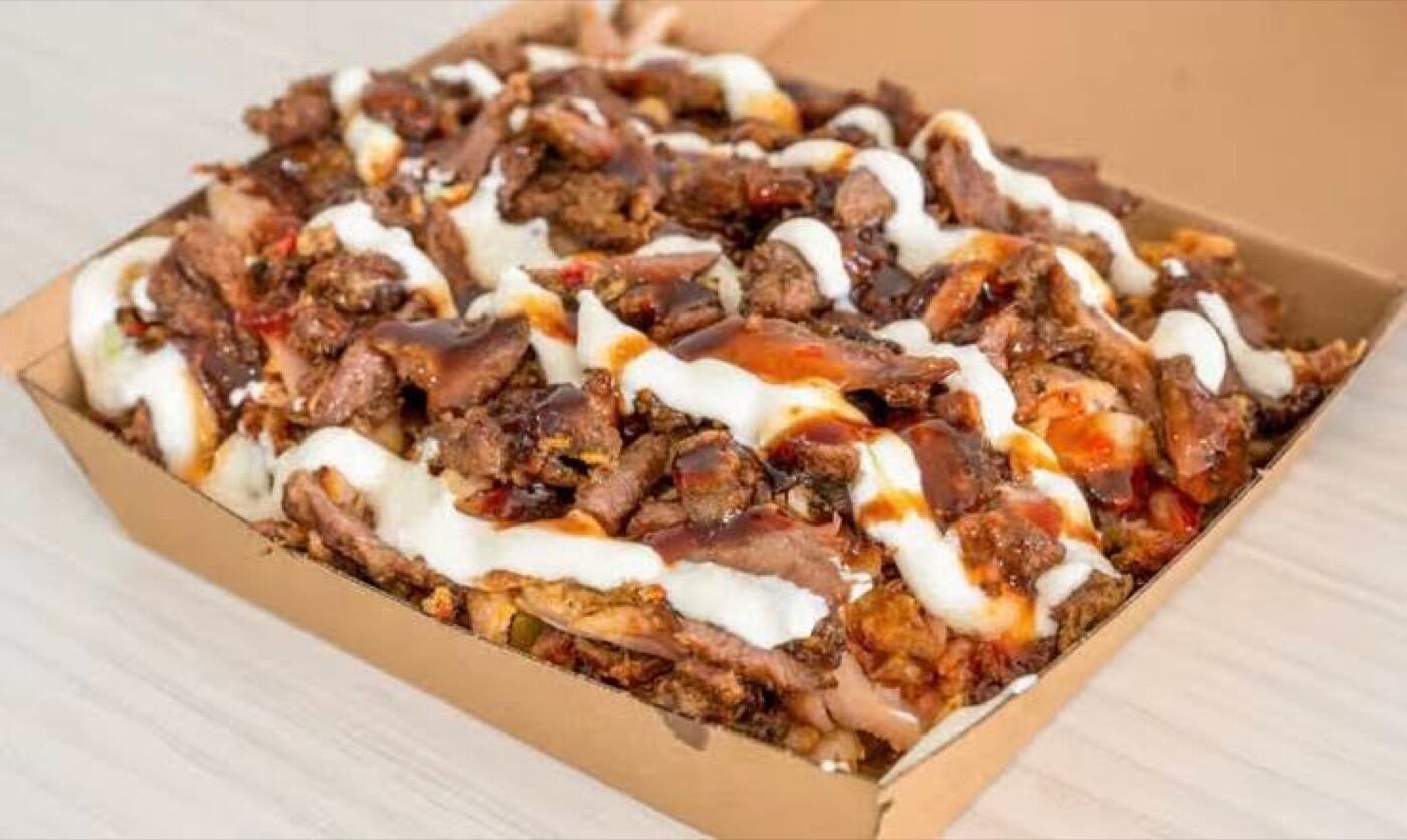 A cardboard tray of chopped grilled meat drizzled with white and red sauces